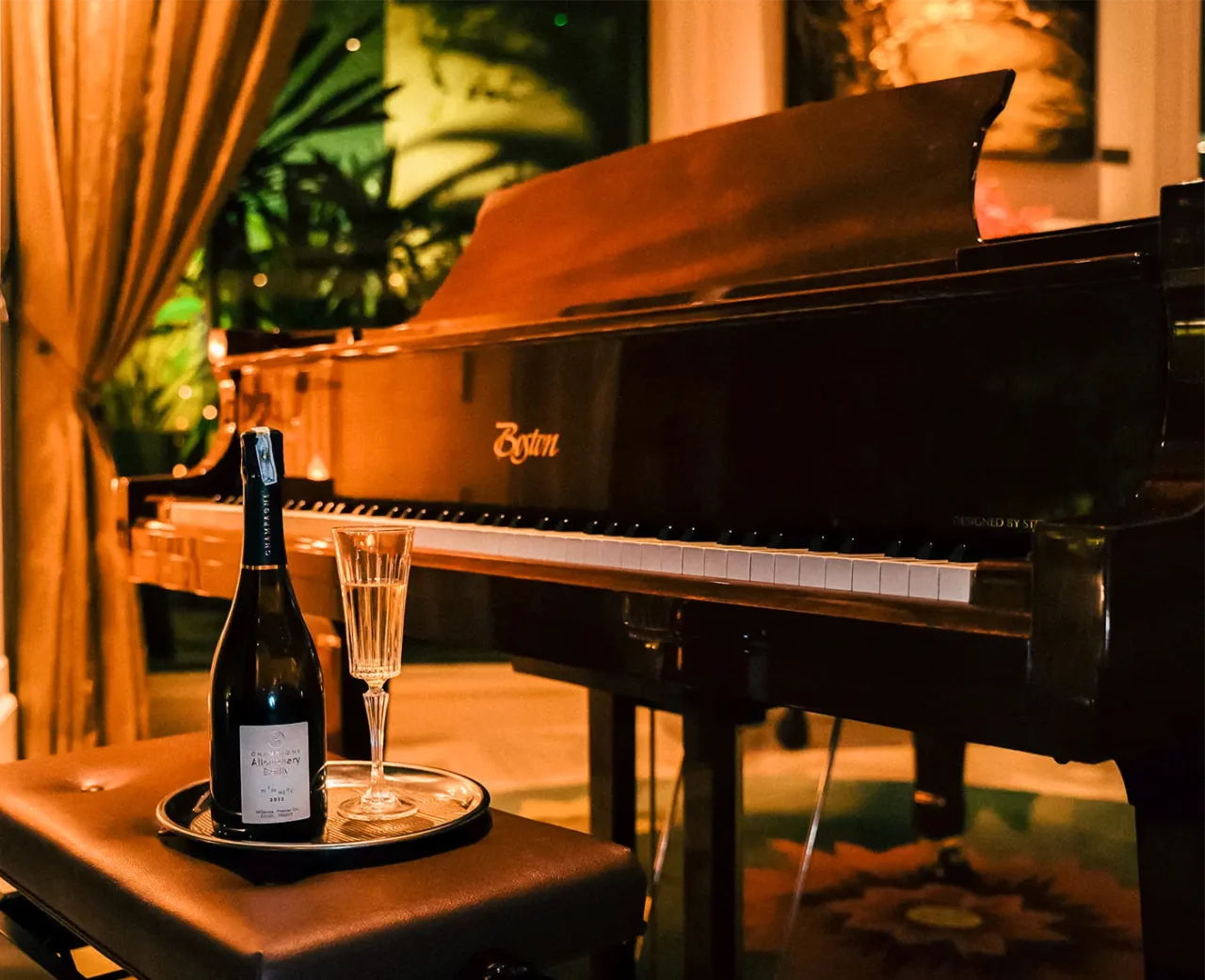 An elegant Boston piano in a subdued atmosphere, accompanied by a bottle of refined champagne and a flute placed on a tray.