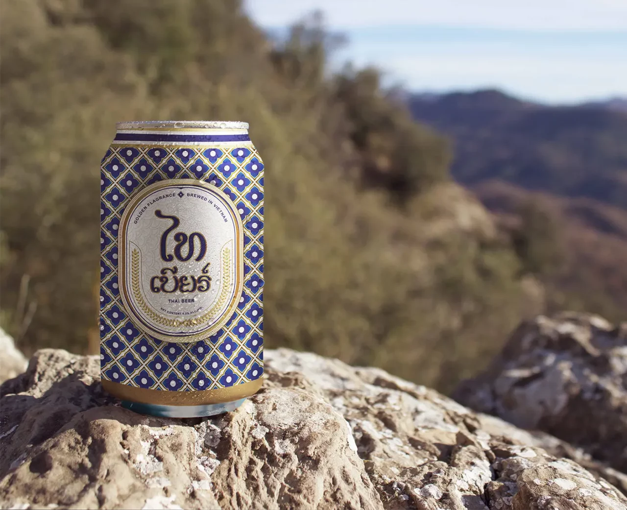 Thai beer can with traditional blue and gold pattern on a rock outdoors.