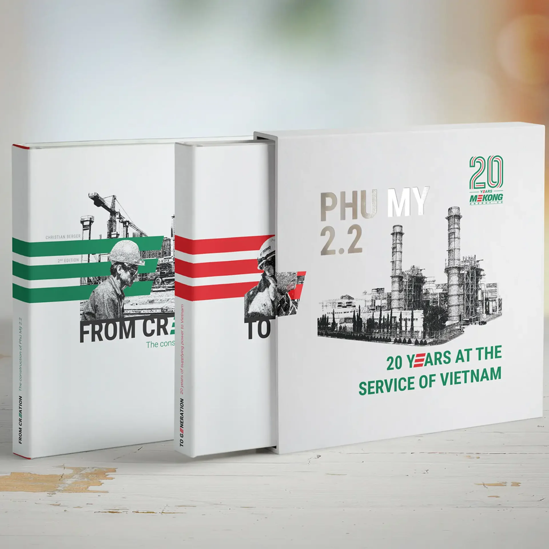 Tres libros conmemorativos sobre la central eléctrica Phu My 2.2, que celebran los 20 años de Mekong Energy con diseños industriales en verde, rojo y plata.