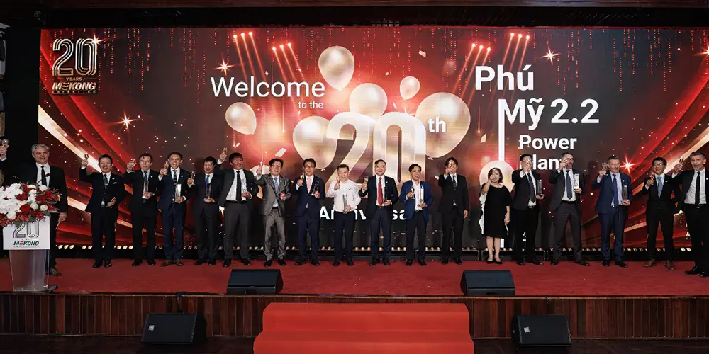 Grupo de personas en el escenario sosteniendo trofeos en la ceremonia del 20º aniversario de Mekong Energy, con una pantalla grande que muestra "Bienvenidos al 20º aniversario: Planta de energía Phú Mỹ 2.2".