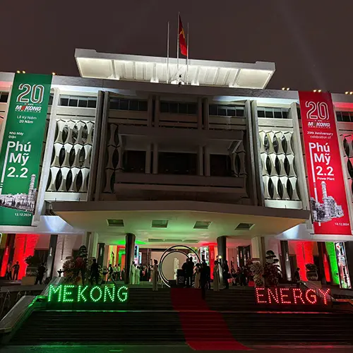 Fachada iluminada de un edificio con pancartas rojas y verdes para el evento del 20º aniversario de Mekong Energy y una alfombra roja que conduce a la entrada.