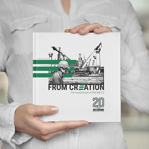 Libro titulado "Desde la Creación - La construcción de Phú Mỹ 2.2", que celebra los 20 años de Mekong Energy, sostenido por una persona con una camisa blanca.