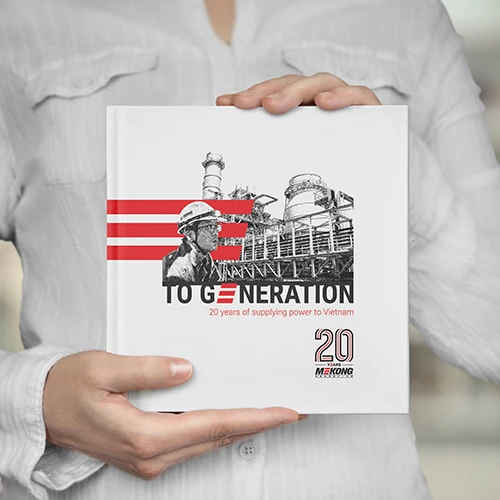 Libro titulado "A la generación: 20 años de suministro de energía a Vietnam", que celebra los 20 años de Mekong Energy, sostenido por una persona con una camisa blanca.